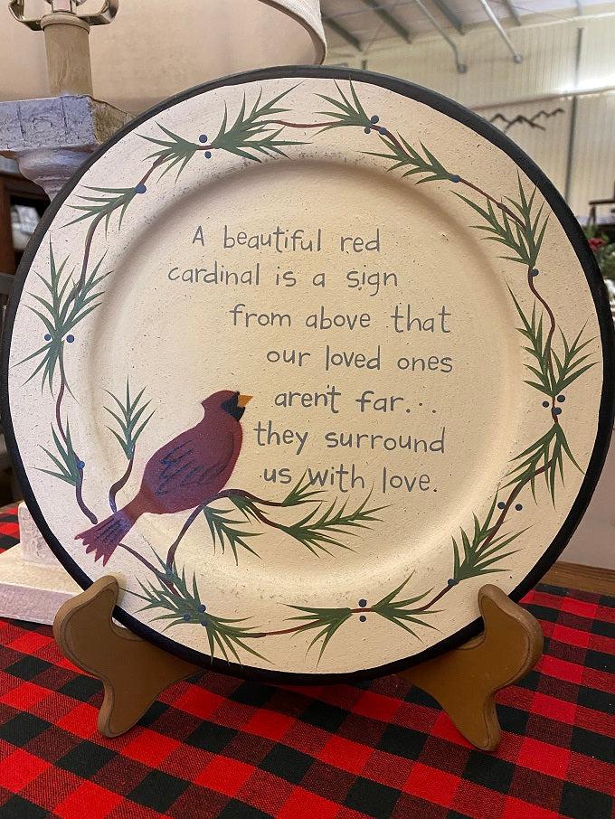 This round wooden plate shows a red cardinal on a cream coloured painted background and features the text:  A beautiful red cardinal is a sign from above that our loved ones aren't far...they surround us with love.