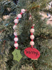 The merry wooden beaded garland is apporximately 19" long and made of white wooden beads alternately with smaller red wooden beads. At one end of the garland is a red wooden medallion with the word Merry painted on it in black lettering. At the other end is holly-like green leaf. 