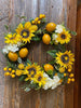 close up of large bright yellow sunflowers and lemons as part of the sunflower lemon floral wreath. The wreath includes pretty white flowers and green leaves as well.
