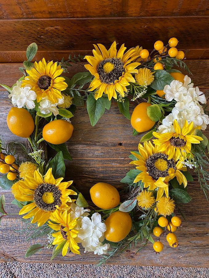 close up of large bright yellow sunflowers and lemons as part of the sunflower lemon floral wreath. The wreath includes pretty white flowers and green leaves as well