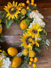 close up of large bright yellow sunflowers and lemons as part of the sunflower lemon floral wreath. The wreath includes pretty white flowers and green leaves as well