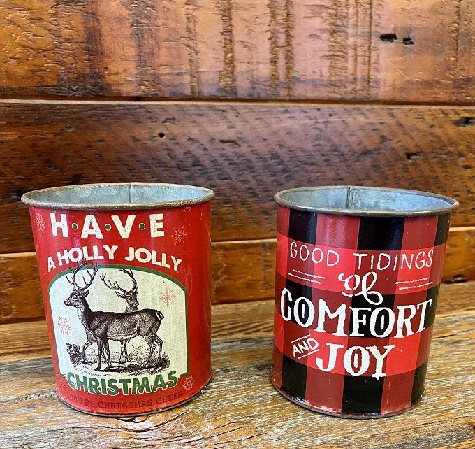 Two styles of the Vintage Christmas cans are shown. One is red and black buffalo plaid and says Good Tidings of Comfort and Joy. The other can has more green tones and says Have a Holly Jolly Christmas with a picture of a pair of reindeer. Both have just a wee bit of distressing in their paint to make them perfectly vintage.