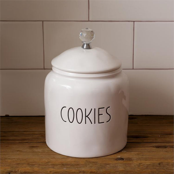White, farmhouse style ceramic cookie container. It has a glass knob on the white ceramic lid. The word Cookies is on one side of the container. 