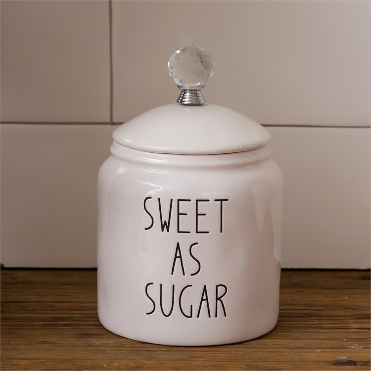  White farmhouse style sugar canister with a glass knob on top of a removable lid. Imprinted on the side of the canister are the words Sweet as Sugar. 