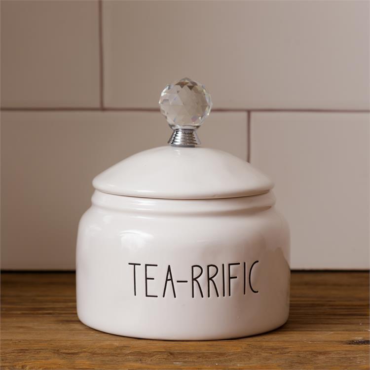 White, farmhouse style ceramic tea container. It has a glass knob on the white ceramic lid. The words Tea-rrific are on one side of the container. 