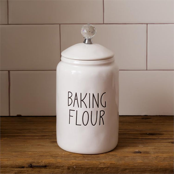 White, farmhouse style ceramic flour container. It has a glass knob on the white ceramic lid. The words Baking Flour are on one side of the container. 