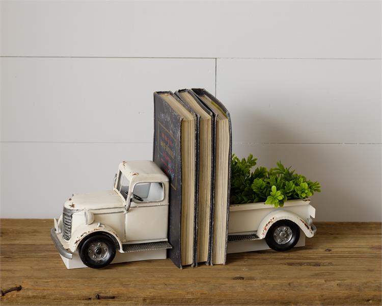 A scaled down model of a white metal truck is cut in half and used a book ends. The truck is white metal and is vintage-styled vehicle. The back of the truck in the photo is filled with faux succulents, but it comes empty.  It would make a great gift for dad on father's day. 