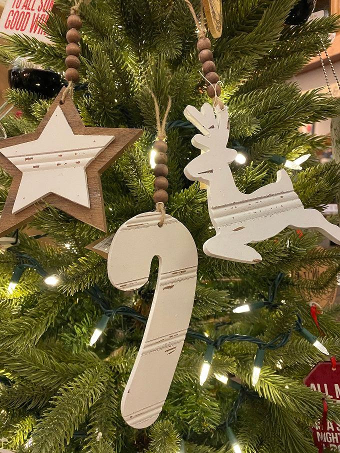 Three Chippy wood ornaments. There is a star, candy cane and a reindeer made of wood and painted and then the wood is distressed for the chipped paint look. The ornaments are white and at the top of each is natural coloured brown beads strung on a jute hanger.