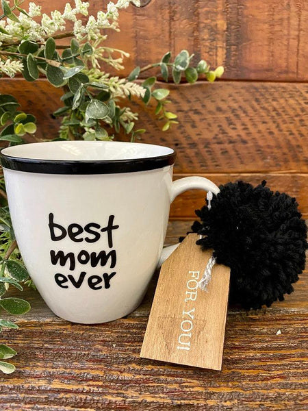 A white ceramic mug ready for gifting with a wooden tag and a black pom pom. Printed in black on both side is the words best mom ever.
