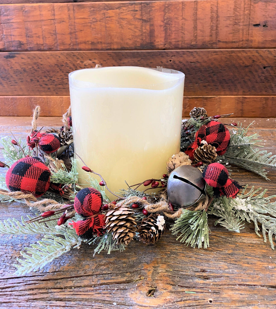 A candle ring from the Country holiday buffalo plaid collection. It is full with red and black buffalo plaid balls in two sizes, silver bells, greenery and pine cones.