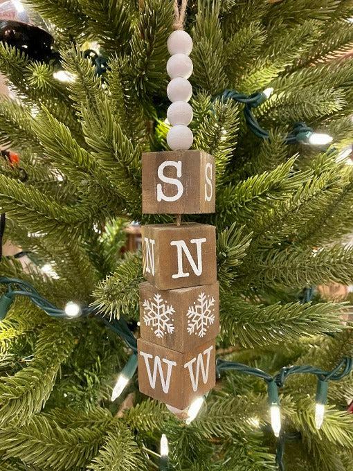 The Beaded Cube Ornament with the word Snow. The natural coloured cubes are printed with a single letter on all four sides and are moveable. White beads are at the top and the bottom of the ornament. 