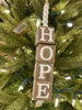 The Beaded Cube Ornament with the word Hope. The natural coloured cubes are printed with a single letter on all four sides and are moveable. Five white beads are at the top and one at the bottom of the ornament. 