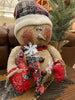 The Happy Burlap Snowman has a red and black plaid hat, is dusted with white snow and is big and round. His face has a big smile and rosy cheeks and there are a few big white snowflakes on his body. 