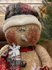 The Happy Burlap Snowman has a red and black plaid hat, is dusted with white snow and is big and round. His face has a big smile and rosy cheeks and there are a few big white snowflakes on his body. 