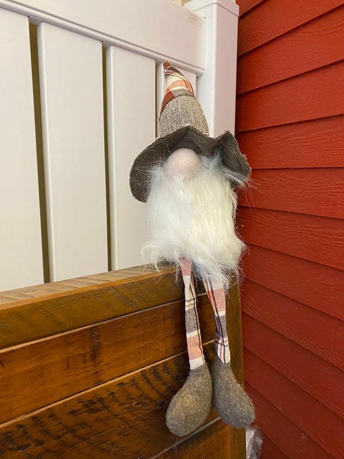 Pictured is a gnome with long dangle legs that will hang loosely. He has a plaid and brown hat with a big brimg and a full bushy beard that wraps around his whole body. 