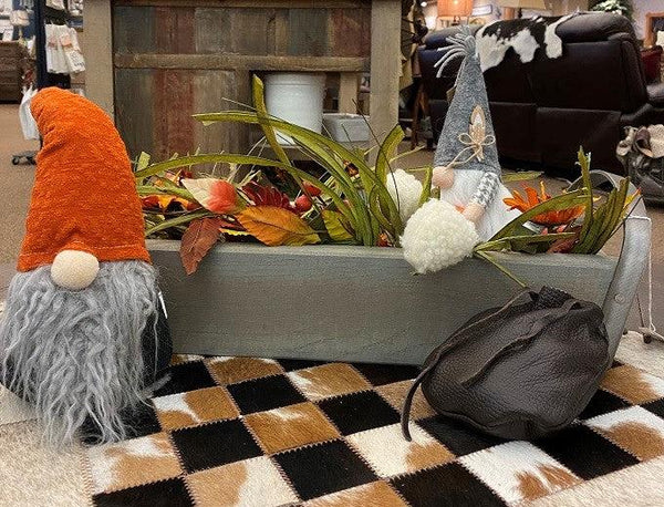 Pictured is a gnome with a weighted bottom so will sit easily on any shelf. He has an orange cap and a full grey beard. He has a black torso. He is shown with a barnboard tray filled with fall greenery . 
