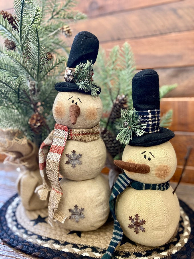 The Green plaid scarf snowman is a twostack snowman and has a black hat with green plaid trim and matching scarf. There  is a jingle bell trim on his hat and one metal snowlake on his bottom stack. The has two twiggy arms. Also shown is the Cranberrry plaid scarf snowman. He has a black hat with jingle bell trims and two metal snowflakes. 
