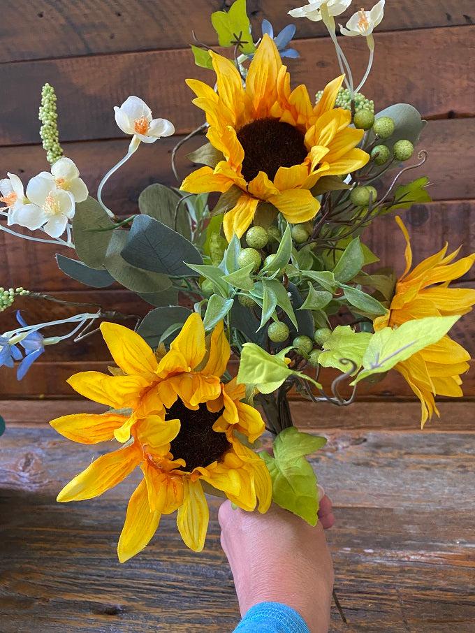 A closeup of the yellow daisy pick. It is a pretty farmhouse pick that is bursting with yellow sunflowers white daisies and green berries. Lots of green leaves fill out this pick.
