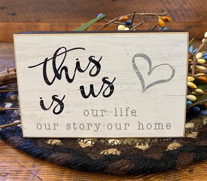 The Family Mini block sign that says: This is us - our life our story our home. The edges are black and the writing is gray and black. 