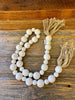 White beaded garland with jute tassels at each end. The beads are white and two sizes that alternate in the strand.