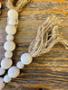 White beaded garland with jute tassels at each end. The beads are white and two sizes that alternate in the strand.