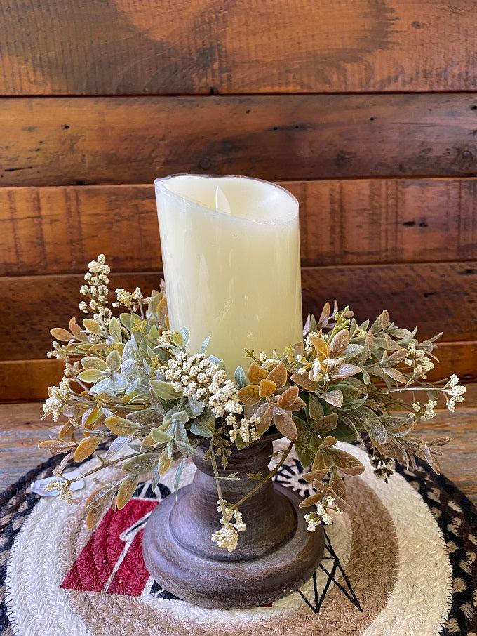 The white weatherly buds candle ring is shown here with an ivory candle and black candle holder. White coloured stems are mixed with soft green shades making for a full candle ring.