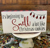 It's beginning to smell a lot like Christmas cookies block sign has a white background, red and black checked edge and It's beginning to smell a lot like Christmas cookies . It has a picture of christmas lights in the top corner. 