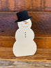 This is a wooden snowman cut out, so shaped like a snowman. It is painted white and its painted features include a black hat, carrot nose, coal for his eyes, nose and buttons.