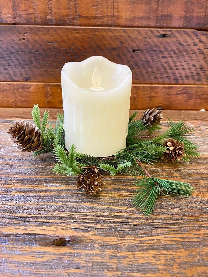 A candle ring made of pine and pine cones around a white LED candle.