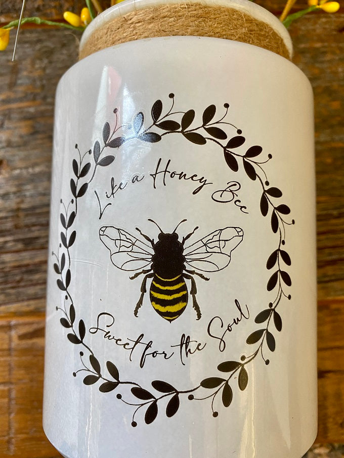 A white glass Honey Bee Jar with a image of a bee surrounded by a black vine of leaves and the words Like a Honey Bee Sweet for the Soul.