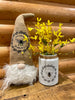 A white glass Honey Bee Jar with a image of a bee surrounded by a black vine of leaves and the words Like a Honey Bee Sweet for the Soul. It is shown with the Honey Bee Gnome.