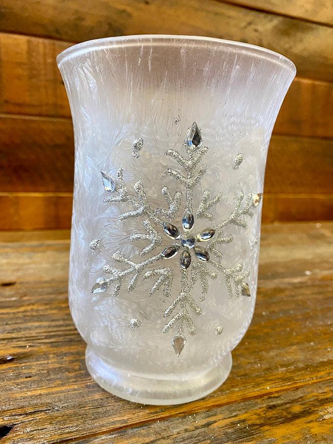 A single frosted white glass hurricane jar have a snowflake pattern in silver on the outside. 