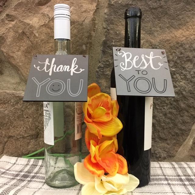 Two wine bottles with You wooden wine tags hanging from the neck of the bottle. One tag is lighter gray and says Best to you on it in white and black lettering. The other tag is darker gray with the words thank you in white and black lettering. The farmhouse wine tags make great gifts. You could write on them with a sharpie and give it as a gift with a bottle of wine. 