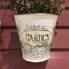A close up of the metal bucket with a flat back so it rests easily against whatever surface you hang it from. The bucket looks weathered and has the word garden embossed on the side.