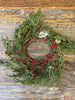 The evergreen pine wreath features green pine like stems, and red berry pips and pine cones. 