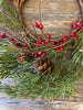 The evergreen pine wreath features green pine like stems, and red berry pips and pine cones.  This is a close up photo.