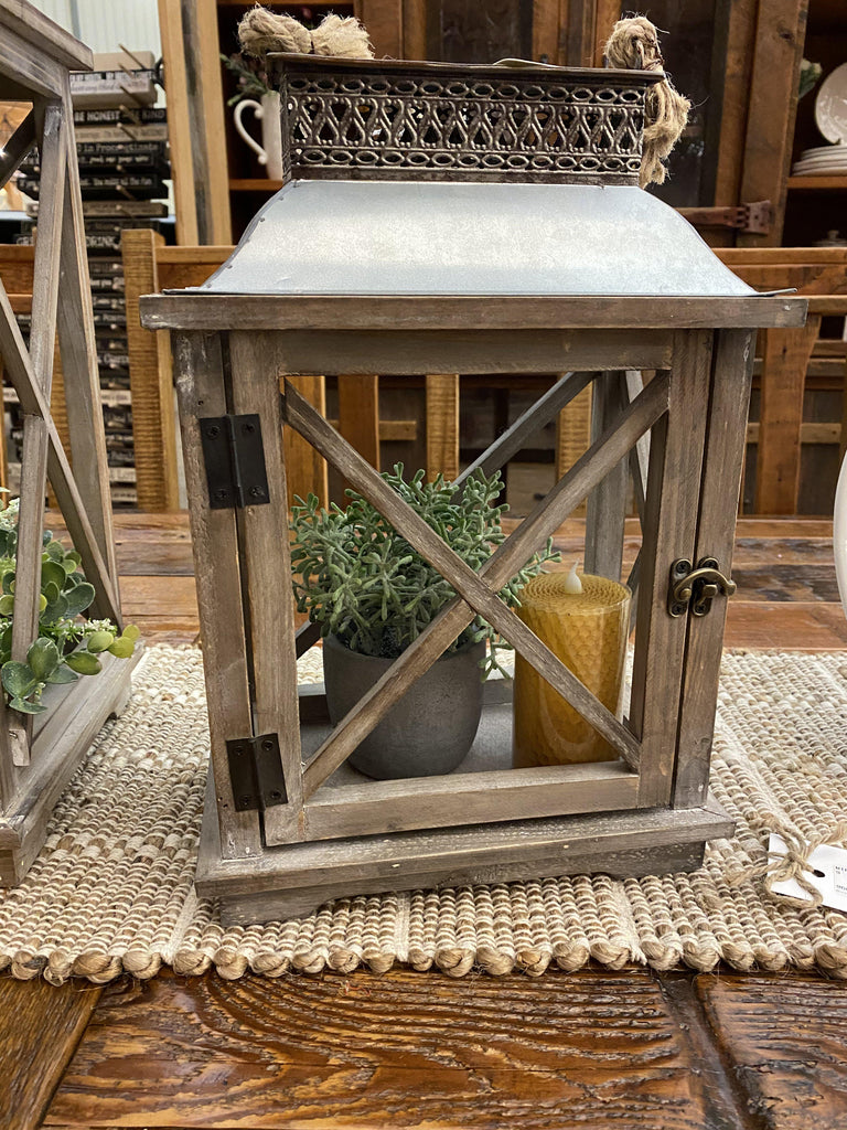 A farmhouse wood and galvanized metal lantern is shown and it is a small pot of greenery and a 4" honeycomb votive pillar candle.