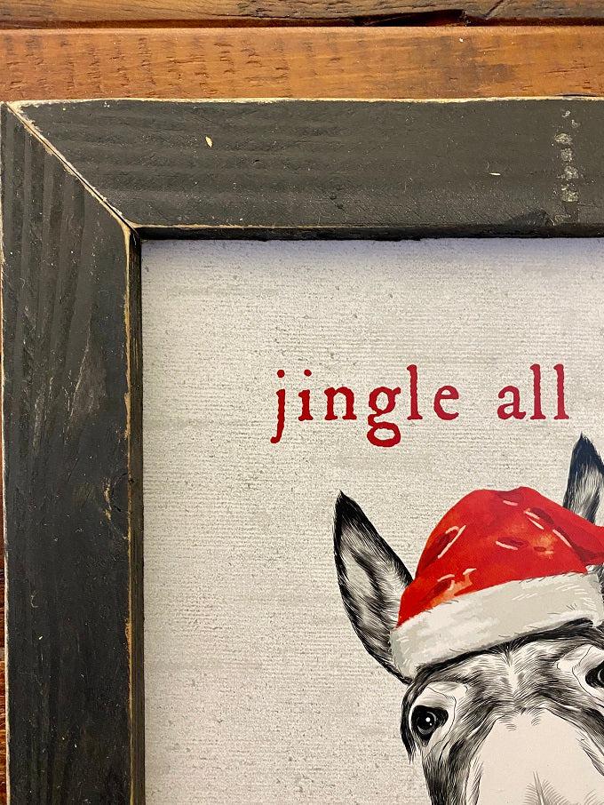 A black and white sign with a donkey wearing a red santa hat staring at you. The words are in red around the donkey say:  Jingle all the Way - no one likes a Half Assed Jingler.  This is a close up of the frame.