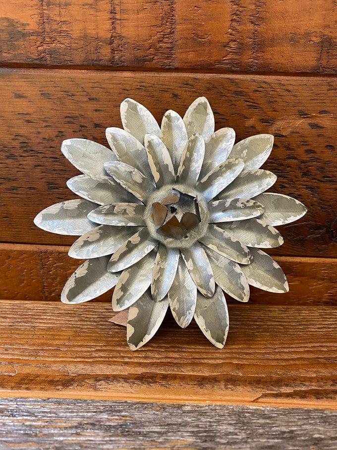 The metal daisy has spikey petals and there are four layers of them. It is made of galvanized metal. The centre of the flower has raised metal pieces coming together for a pretty centre. There is a white distressed paint o the tips of the petals.