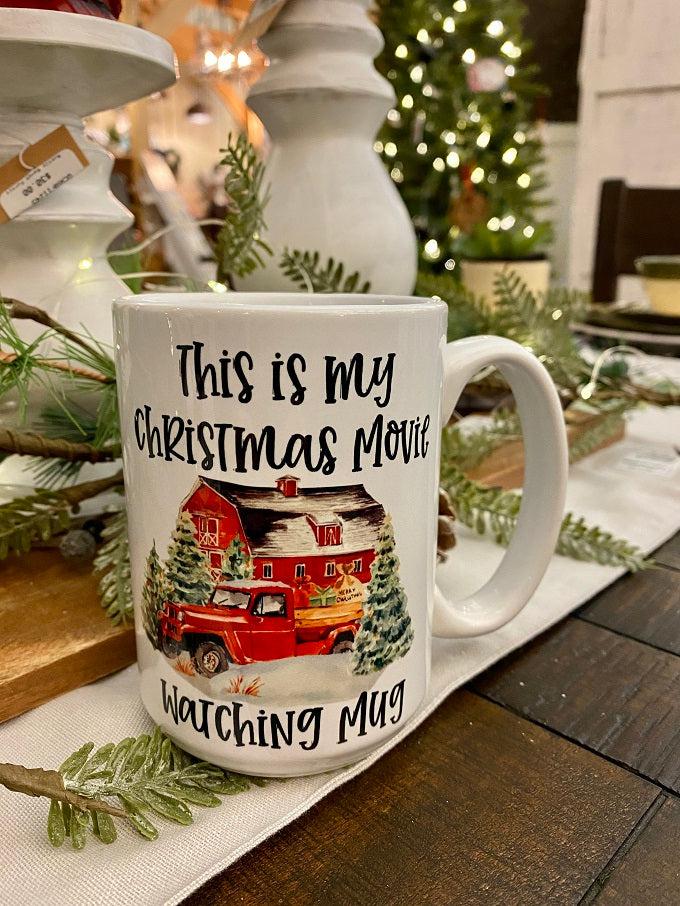 This is a white ceramic mug printed with the words "This is my Christmas movie watching mug" and a red barn, red truck and evergreen trees in a snowy holiday scene. 