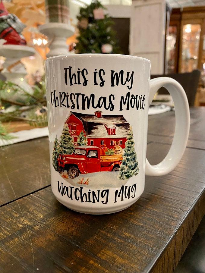 This is a white ceramic mug printed with the words "This is my Christmas movie watching mug" and a red barn, red truck and evergreen trees in a snowy holiday scene.