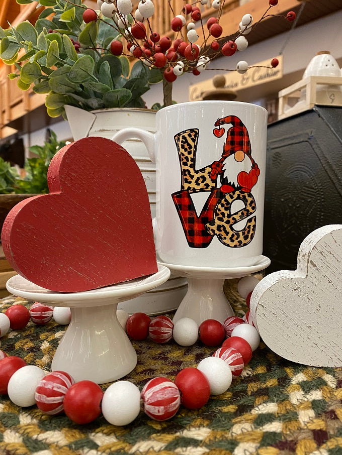 The Love Gnome mug is shown with other valentine decor. The gnome on the mug has a red and black buffalo plaid hat. The V of Love is also Red and Black Buffalo plaid and the L and E are leopard print.