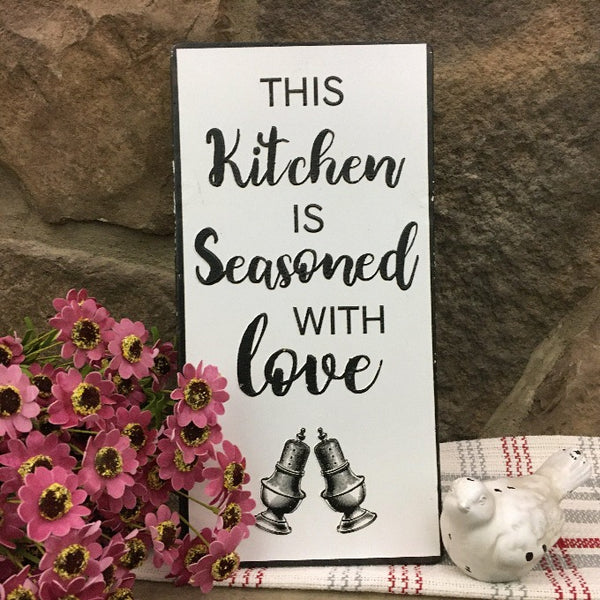 Seasoned with Love Kitchen Sign is a metal sign with black writing and image of salt and pepper shakers.