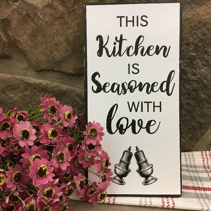 Seasoned with Love Kitchen Sign is a metal sign with black writing and image of salt and pepper shakers.