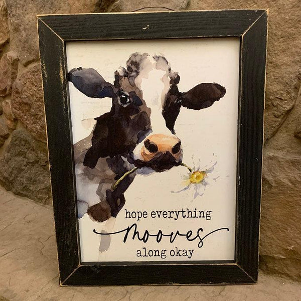 This sweet bathroom print has a watercolor black and white cow with a white daisy in her mouth and reads, "hope everything mooves along okay." It is in a black wooden frame with light distressing.