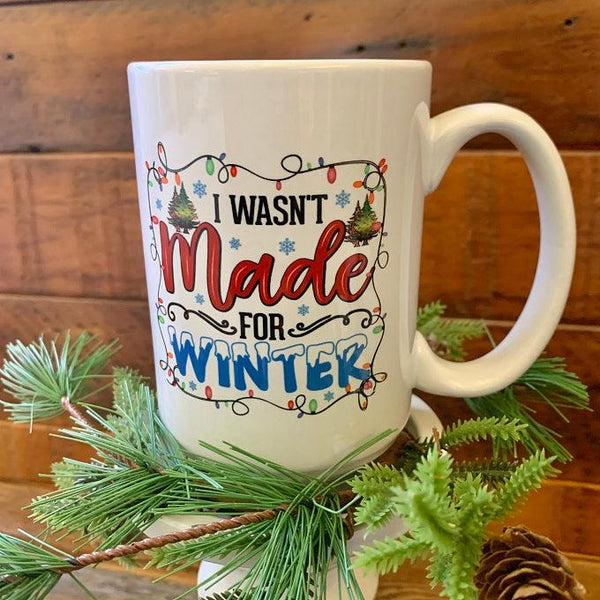 This is a white ceramic mug that is printed on both sides with the saying I wasn't made for winter in a colourful font.