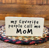 It is a wooden sign with a white edge covered in tiny black hearts. My favorite people call me mom is printed in black