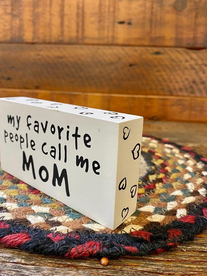 It is a wooden sign with a white edge covered in tiny black hearts. My favorite people call me mom is printed in black