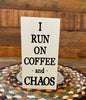 It is a wooden sign with a black and white striped edge. I Run on Coffee and Chaos is printed in black