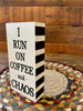 It is a wooden sign with a black and white striped edge. I Run on Coffee and Chaos is printed in black. This sign shows the black and white striped edge.
